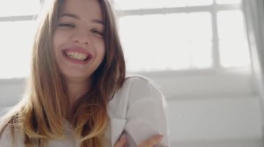 Şık bir iç mekanda güneşli bir sabahın tadını çıkaran mutlu genç kadın. Işıl ışıl gülümseyen neşeli genç bir kadın. Parlak, güneşli bir odada uzanıyor. Mutluluk ve rahatlık saçıyor..