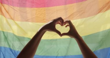 Gay and lesbian pride lgbt flag. Supporting hands make heart sign and wave in front of a rainbow flag flying. Love sign. Celebration Event Symbol Of LGBT. Love Equal. LGBT rights. human relationships.
