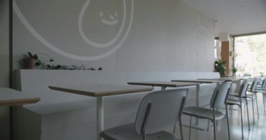 Minimalist tasarımı, ahşap masaları ve beyaz sandalyeleri olan modern bir kafe. Büyük bir fincanın duvar resmi eğlenceli bir dokunuş katıyor. Modern yemekle ilgili konular için ideal