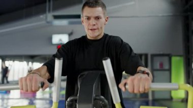 Modern iç mekanları olan bir spor salonunda yoğun bir şekilde direniş eğitimi alan genç bir adam. Modern Spor Salonu 'nda Direniş Makinesi Kullanan Genç Adam