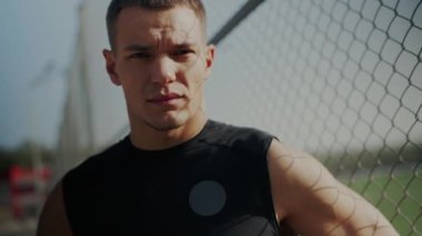 Atletik bir adam tel örgülere karşı dinleniyor, antrenmanına ara veriyor, kararlılığını ve dikkatini gösteriyor. Odaklanmış Spor Giyimi Duraklama: Zincir Bağlantı Çiti