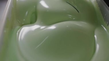 Yeşil jelatin tatlısının parlak, kaygan yüzeyini gösteren, kıvrımlarını ve parıltılarını vurgulayan makro bir çekim. Yeşil Jelatin Tatlının Pürüzsüz Dokuya Yakın Çekimi