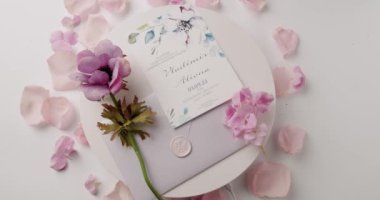 Pembe taç yaprakları ve güzel bir çiçek aranjmanıyla çevrili beyaz bir arka plana karşı güzel tasarlanmış bir düğün davetiyesi. Zarafet ve romantizmi temsil etmek için mükemmel. Zarif Davet