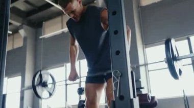 Çağdaş bir spor salonunda ağırlık kaldıran odaklanmış bir adam idman sırasında azim ve fiziksel güç gösteriyor. Modern Spor Salonunda Halter ve Spor Ekipmanı