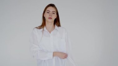 Beyaz gömlekli ve ceketli bir kadın beyaz bir arka planın önünde duruyor. Dirseği belinde duruyor ve bir moda etkinliğinde baş parmağıyla el kol hareketi yapıyor.