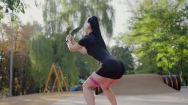 Odaklanmış genç bir kadın dingin bir park ortamında yoğun bir spor yapıyor, sağlığa ve sağlığa olan bağlılığını gösteriyor. Park 'ta Açık Hava Spor Programı Yapan Genç Kadın