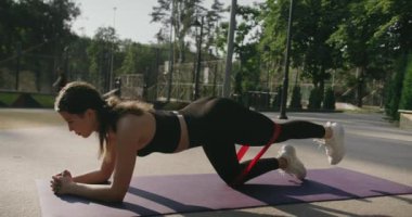 Yoga tahtası pozu veren bir kadın. Direniş bandıyla egzersiz yapan genç bir kadın. Spor kıyafetli kadın bacaklarını eğiyor ve elastik direnç bantlarıyla vücut geliştirme egzersizleri yapıyor..