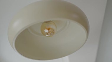 Modern, krem rengi bir lambanın yakın plan görüntüsü. İçinde Edison ampulü var. Basitlik ve zarafet, hem ev hem de ofis ortamları için uygun bir minimalist dekor cazibesi sunuyor. Modern Krem Lambası