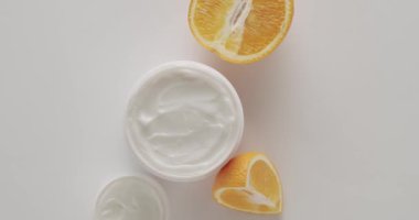 Saç ve cilt bakımı için doğal kozmetik ürünleri. Kremalı parlak kozmetik kavanozu. Kavanozlar, portakal meyveli şişeler ve kozmetik ve güzellik tedavisi için tüpler beyaz arka planda dönüyor. Üst Görünüm.