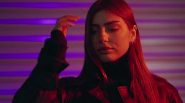 Gece vakti renkli arka planda kameraya bakan genç, lüks, seksi bir kadın. Canlı neon renkli ışıklarla aydınlatılmış baştan çıkarıcı bir kadının portresi. Güzel kız kameraya bakıyor..