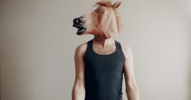 At maskeli komik bir adam evde beyaz arka planda el eğitimi için ağırlık egzersizi yapıyor. Evde komik bir spor salonu var. Esprili esnemeler. Komik ev egzersizi.