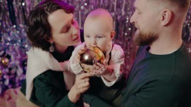 Mutlu bir aile yeni yılı kutluyor. Anne ve baba ve bebek Noel süsü tutuyorlar. Neşeli atmosfer ve mutluluk. Aile Yeni Yılı Bebek Tutma Noel süsüyle kutluyor