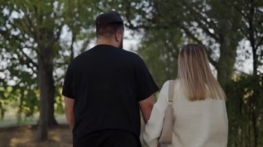 Bereketli bir parkta yürürken, genç bir erkek ve kadını arkadan yakalayan huzurlu bir görüntü, bir arkadaşlık duygusunu ön plana çıkarıyor. Genç Çift Bir Resim Parkı 'nda Birlikte Yürüyor
