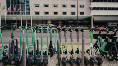 Arka planda sürdürülebilir kentsel ulaşımı temsil eden modern çok katlı bir bina olan şehir kaldırımına düzgün park edilmiş bir sıra yeşil elektrikli scooter ve motosiklet..