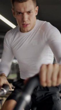 Kapalı alan bisikleti üzerinde sıkı çalışan kararlı bir yüz ifadesi olan genç bir erkek atlet. Terleme ve yoğunluk onun çalışmasını tanımlar. Bir Spor Salonu Bisikletine Yoğun Odaklanmış Genç Adam Eğitimi