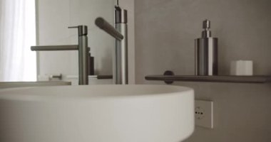 Modern lavabosu ve parlak metal musluğu olan şık minimalist bir banyonun yakın çekimi, temiz ve zarif bir tasarımı sergiliyor. Modern Minimalist Banyo İçi. Stil Lavabo ve Musluk Tasarımı