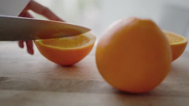 Ahşap bir yüzeyde taze portakallar kesen bir elin yakın plan çekimi, canlı rengi ve dokuyu vurguluyor. Sağlıklı beslenme, tazelik ve yemek pişirmeyle ilgili kavramlar için mükemmel..