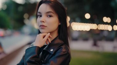 Deri ceketli özgüvenli bir kadının portresi. Arka planda bokeh ışıkları var. Akşam atmosferi biraz sıcaklık ve gizem katıyor. Deri ceketli kendine güvenen kadın.