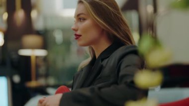 Modern bir şehir kafesinde oturan kırmızı rujlu ve sarı saçlı zarif genç bir kadın. Ayarlama, entellektüellik ve güven hissi veriyor. Modern Şehir Kafesinde Rahatlayan Kendine Güvenen Genç Kadın