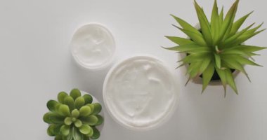 Kozmetik ürünleri için yeşil yapraklı beyaz kavanozlar ve tüpler stüdyoda beyaz bir arkaplanda dönüyor. Doğal malzemelere dayalı kozmetik yağları, fırça, tonik, vücut bakımı. Farklı kozmetik şişeleri.