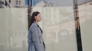 Şehir manzarasına yansıyan profesyonel bir genç kadın, şehir ortamında düşünceli ve sakin görünüyor. Şehrin Yansımalarına Karşı Düşüncede Genç Profesyonel Kadın