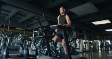 İyi donanımlı, geniş bir spor salonunda koşu bandı kullanan odaklanmış genç bir erkek atlet. Günlük fitness rutininin ve dayanıklılığın özünü yakalar. Modern Spor Tesisinde Koşu bandında Koşan Genç Adam