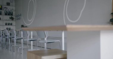 Tarafsız tonlarda minimalist bir tasarımın yer aldığı modern bir kahve dükkanının sakin bir fotoğrafı. Temiz, dağınık alan beyaz sandalyeler, basit bir ahşap bar ve ince duvar süslemeleri içerir.