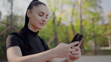 Parkta akıllı telefonunu kullanan atletik giysili genç bir kadın. Doğal ortamda bir fitness başvurusunu kontrol ediyor. Smartphone Açık havada Aktif Kadın Fitness Uygulaması