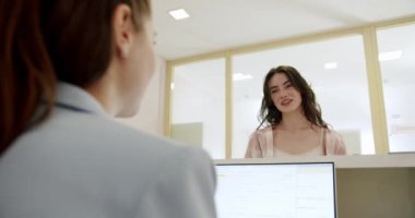 Genç profesyonel bir kadın ofis tezgahında durup meslektaşıyla konuşuyor. Görüntü, modern ofis ortamında dostane bir iş etkileşimi yakalıyor..