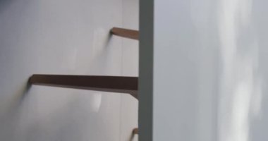 Çağdaş minimalist bir iç mekânın yakın bir görüntüsü. Beyaz dokulu bir duvara karşı parlak ahşap bir raf. Basitliği ve tarzı somutlaştırıyor. Minimalist İç Tasarım. Dikey video.