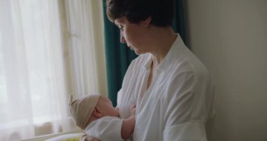 Anne kadın bebeği elinde tutuyor. Anne onu kollarına alarak bir bebeği sallayarak sakinleştirmeye ve uyutmaya çalışıyor. Anne kucağında sallanan bebek usulca gülümsüyor bebeği yatağına yatırıyor..