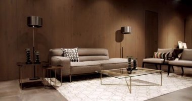 İskandinav iç mimarisi, ahşap duvar, modern gri ve bej kumaş kanepe. Yastıklı tekstil döşeme kanepesi. Modern apartman güzel bej kanepe modern oturma odasında lamba ve halı, masa.