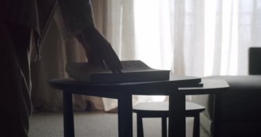 İçinde zarif perdeleri olan bir pencerenin yanındaki sehpanın üzerinde kitap bulunan rahat bir ev sahnesi. Rahatlama, okuma ve huzurlu bir yaşam alanı kavramları için idealdir..