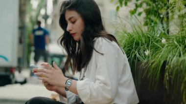 Şehir parkında bir bankta oturan, doğa ve yeşillik içinde akıllı telefonuyla mesajlaşan genç bir kadın. Şehir parkında mesajlaşan genç kadın, doğayı rahatlatıyor ve eğlendiriyor.