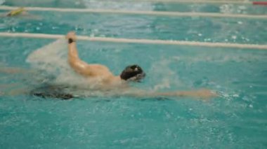 Odaklanmış bir erkek yüzücü, kapalı bir yüzme havuzunda serbest stil felçle suda süzülür. Yetenek ve kararlılık gösterir. Erkek Yüzücü Kapalı Havuzda Serbest Yüzme Uygulaması