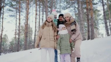 Beş kişilik neşeli bir aile, karlı bir ormanda el ele yürüyor, gülümsüyor. Aşkı, sıcaklığı ve kış eğlencesini yakalamak için mükemmel bir an. Mutlu Aile Ormanda Karlı Günün Tadını Çıkartıyor