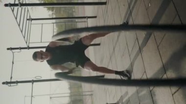 Modern bir spor salonunda yoğun süspansiyon eğitimi alan odaklanmış bir erkek sporcu. Kentsel fitness antrenman sahnesi. Şehirdeki Spor Salonu 'nda Atletik Adam Eğitimi. Dikey video.
