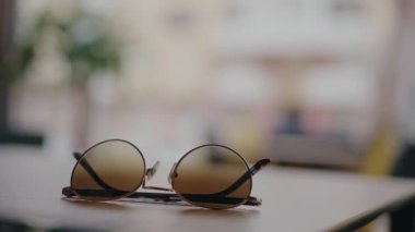 Arka planı bulanık bir masada dinlenen şık güneş gözlüklerinin yakın çekimi, sıcak ve rahat bir ev ortamını çağrıştırıyor. Tahta Yüzeyde Yuvarlak Güneş Gözlüğü Yumuşak Bulanık Arkaplan