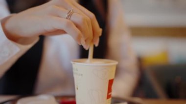 Tek kullanımlık bir fincanda kahvesini karıştıran, yüzükle süslenmiş bir kadının ellerini yakalayan yakın plan bir resim. Huzur dolu bir anı ön plana çıkarıyor. Bright Cafe 'de Kadın Takviyesi Karıştıran Yakın Çekim Kahve