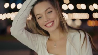 Geceleri gülümseyen mutlu bir kadının yakın çekimi. Işıklardan oluşan güzel bir arka planı var. Güzel Bokeh Arkaplanlı Mutlu Kadın Geceleri Gülümsüyor. Güzel Kadın Pozisyonu