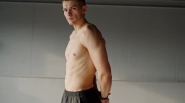 Modern bir spor salonunda kendinden emin bir şekilde duran genç adam. Kaslı bir vücudu olan odaklanmış genç bir adam modern bir spor salonunda duruyor ve idmandan sonra özgüven ve kararlılık yayıyor..