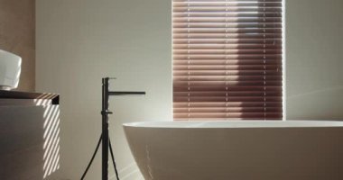 Serbest banyo küveti, parlak fayanslar ve yumuşak gölgeler bırakan Venedik panjurları olan modern bir banyo. Sakin ve minimalist bir tasarım. Serbest Küvetli Modern Tuvalet