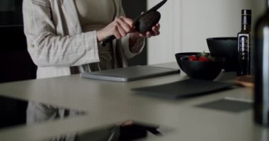 Mutfak tezgahında, taze sebzelerle avokado dilimleyen bir kadının modern bir mutfak ortamında sağlıklı yemek pişirmenin özünü yakaladığı yakın plan. Taze Avokado Hazırlayan Kadın