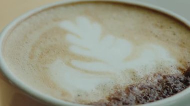 Beyaz seramik bardakta servis edilen nefis bir latte 'nin yakın plan görüntüsü. Kahve severler ve kafe atmosferleri için mükemmel. Yaprak Tasarımlı Latte Sanat Kahvesinin Yakın Çekimi 