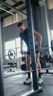 Genç adam spor salonunda yoğun bir halter egzersizi yapıyor. Gözle görülür ter ve çabayla odaklanmış ve kararlı çalışma oturumu. Spor salonunda Halter Egzersizinde Yoğun Egzersiz Dikey