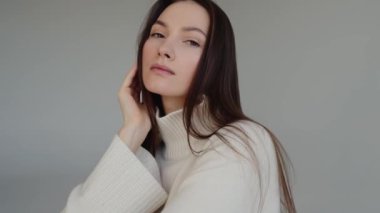 Beyaz kazaklı bir kadının bir resim için poz verdiği anı yakalayan bir video. Kameraya bakan güzel bir kızın portresi.