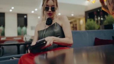 Güneş gözlüğü takan, şık bir kıyafet giyen, modern bir barda eğlenen, kendine güveni ve tarzı olan şık bir kadın. Modern Lounge Bar 'da keyif çatan güneş gözlüklü şık kadın.