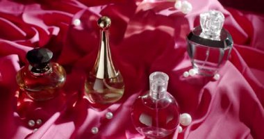 Süslü incilerle süslenmiş pembe bir kumaş üzerindeki zarif parfüm şişelerinin güzel bir düzenlemesi. Görüntü lüks, zarafet ve entelektüellik hissi uyandırıyor..