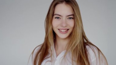 Uzun sarı saçlı, neşeyle gülümseyen, tarafsız bir arkaplanda günlük beyaz gömlek giyen genç bir kadının portresi. Beyaz gömlekli neşeli bir şekilde gülümseyen genç kadın.