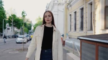 Şehir caddesinde rahat bir şekilde yürüyen genç bir kadın. Rahat bir atmosferi olan kentsel bir ortam. Binalar ve yeşillik dengeli bir zemin sağlar. Sokakta Dolaşan Kadın Sıradan Kıyafetlerle